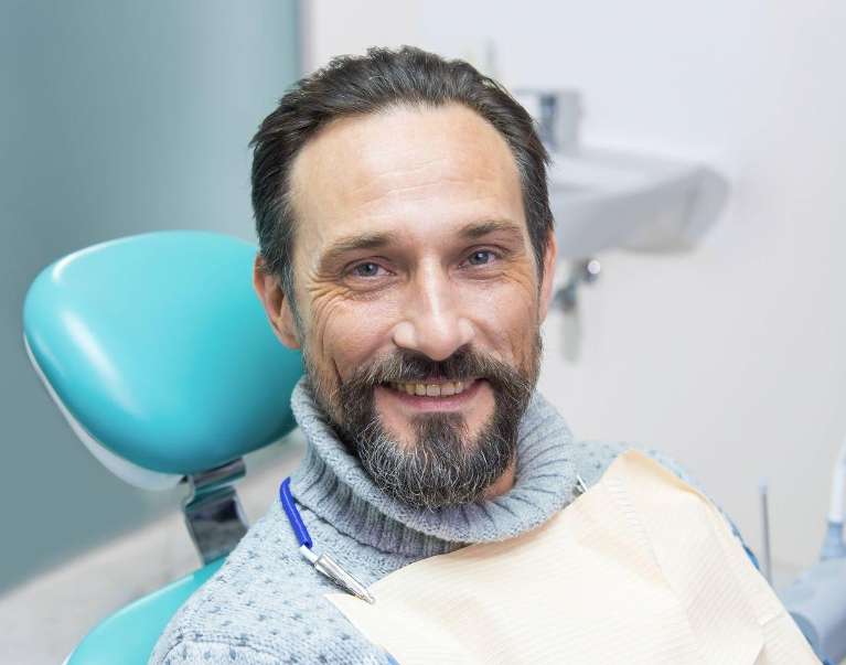 man sitting in exam chair smiling | prosthodontist cleveland